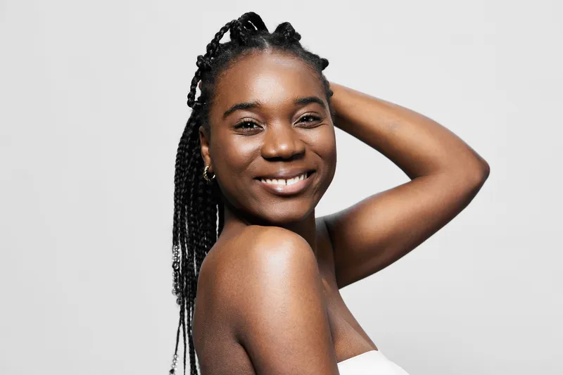 Beautiful smiling Black woman with braided hair, posing against a light background, showcasing natural beauty and confidence