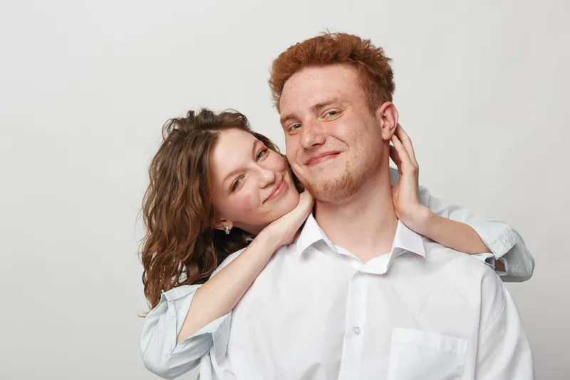 Happy young couple with curly hair and red hair smile and embrace each other on white background. Concept of love, relationship, friendship, and positive emotions between people.