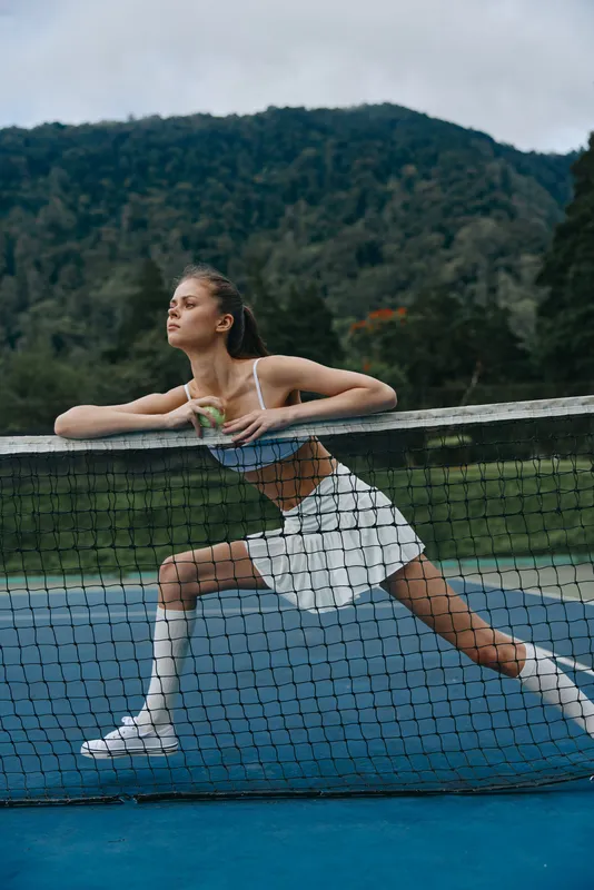 Young athletic woman in sporty attire posing on a tennis court, showcasing determination and strength against a natural background