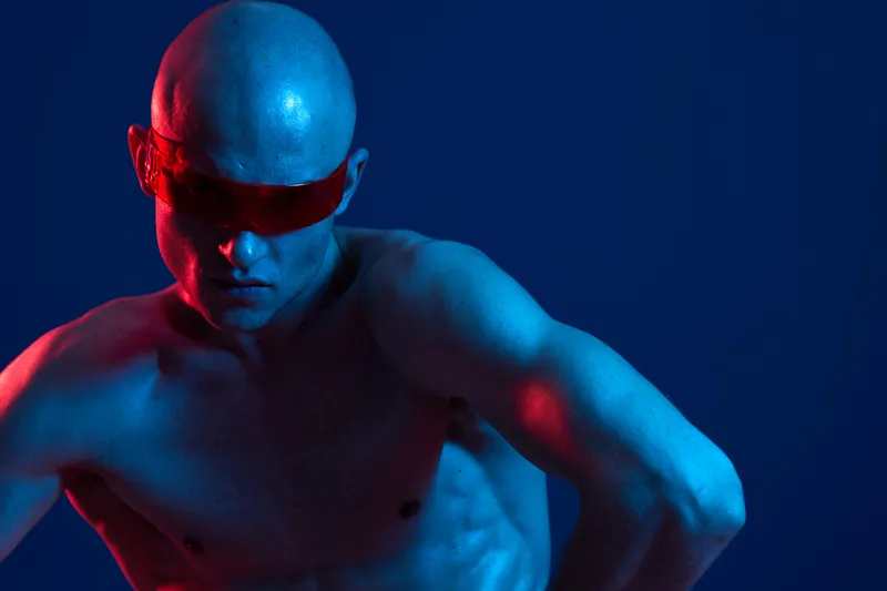 A striking image of a man in sunglasses, showcasing an intense expression and accentuated features under dramatic blue and red lighting.