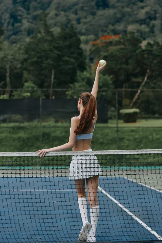 Young female tennis player preparing to serve on a sunny outdoor court, showcasing athleticism and determination in a vibrant green surroundings
