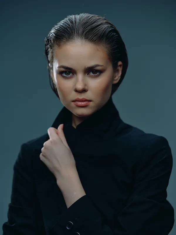 serious woman with slicked hair wearing black clothing in studio light, confident expression, dark background