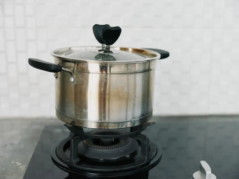 Металлическая кастрюля со стеклянной крышкой стоит на электрической плите на кухне