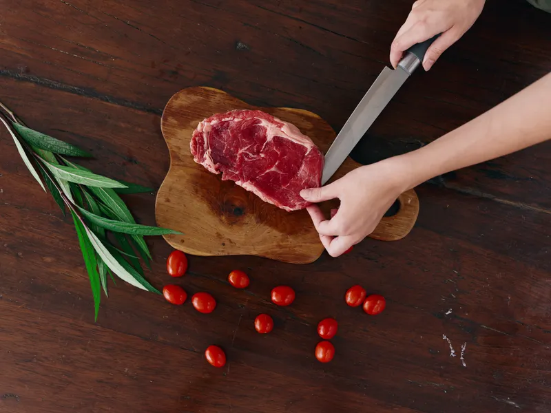 Женщина с ножом в руке нарезает свежее стейковое мясо для жарки на кухне