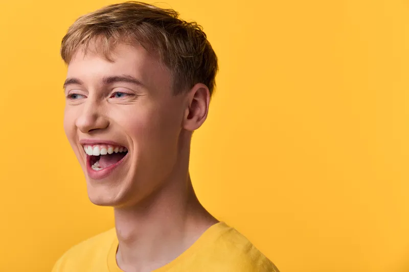 Smiling, laughing young male with casual tee against a bright yellow background, conveying cheerful mood, studio lighting and energetic expression for lifestyle, positive branding or advertising