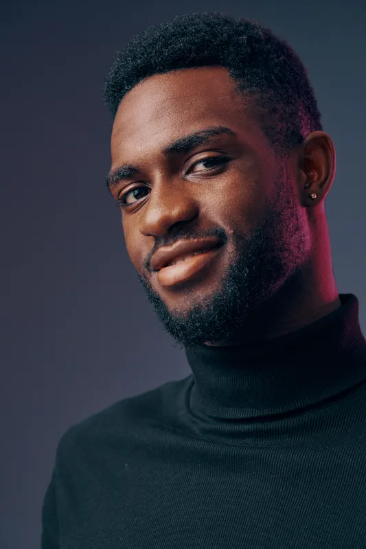 Portrait of a confident young Black man smiling, wearing a black turtleneck sweater, against a colorful gradient background showcasing vibrant emotions
