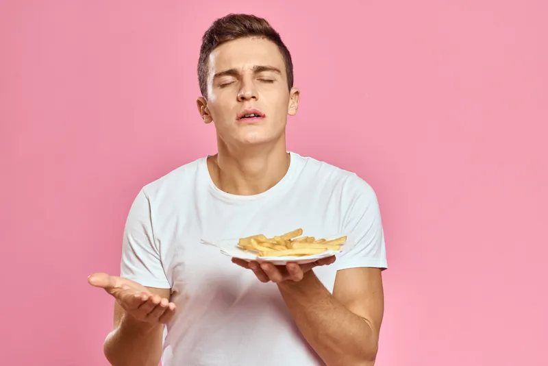Мужчина с картофелем фри в бумажной коробке на розовом фоне, калории, фастфуд, портрет