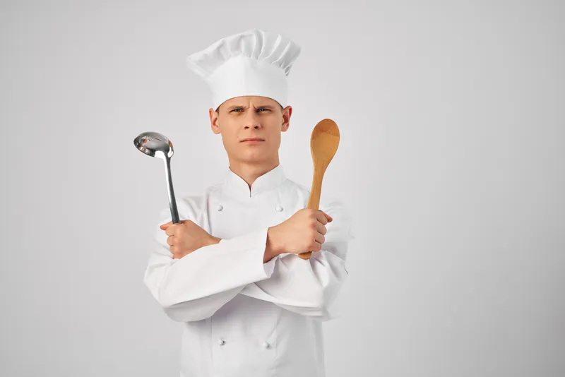 Мужчина в форме шеф-повара работает на кухне ресторана, используя кухонные принадлежности