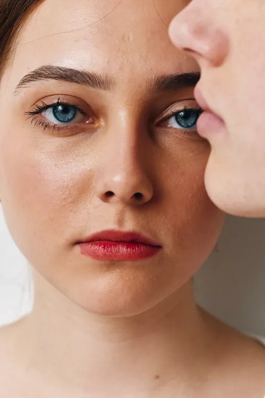Woman portrait with blue eyes and red lips closeup, showing natural skin texture and serious expression. Female face, clear complexion and makeup details in soft light studio environment.