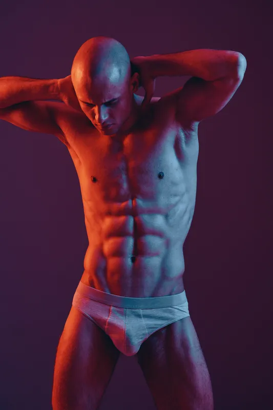 Athletic man posing with dramatic light, showcasing his toned physique against a colorful background. Black and white elements enhance the visual contrast and impact.