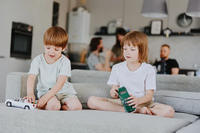 Two happy boys play with toy cars in a cozy modern living room, creating joyful moments together, surrounded by cheerful energy and soft colors.
