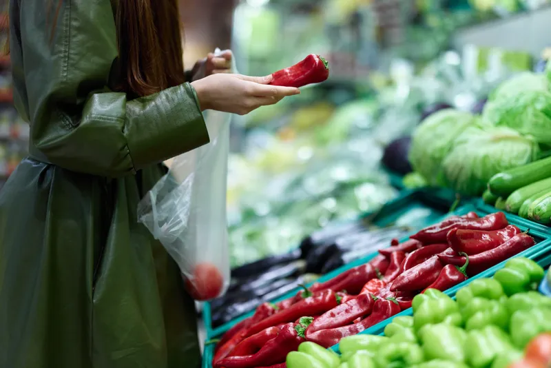 Женщина в продуктовом магазине выбирает свежие овощи, чтобы приготовить ужин, совершает покупки