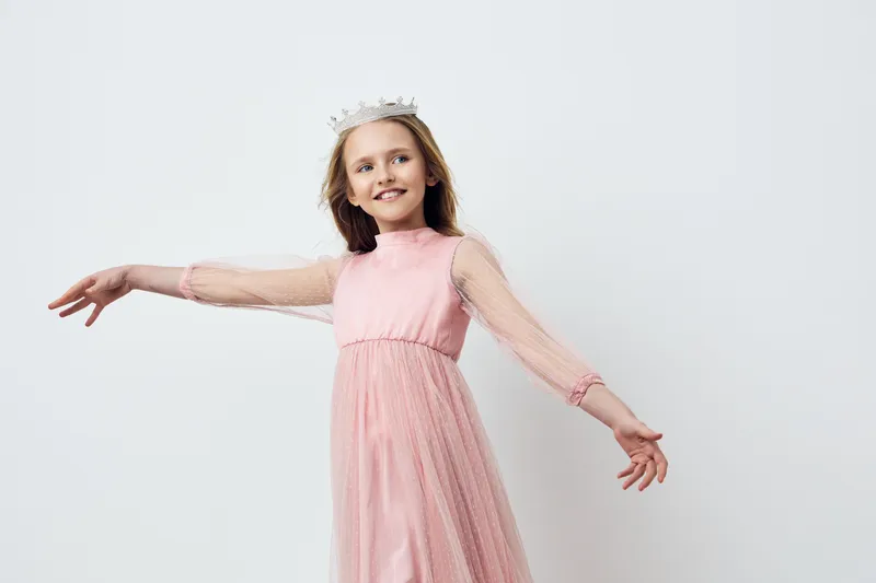 Happy girl in a pink dress with a crown, twirling joyfully against a clean white background, perfect for celebrating childhood and special occasions