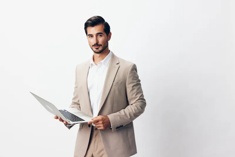 Улыбающийся мужчина-фрилансер в деловом костюме сидит с ноутбуком в бежевом офисе