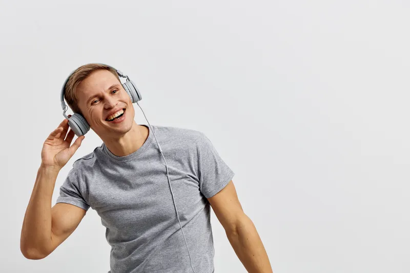 Smiling young man listening to music with headphones, casual grey t-shirt, enjoying music, cheerful expression, isolated on plain white background, studio portrait, lifestyle concept, happy mood