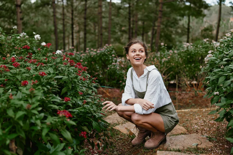 Happy young model enjoying nature in a garden full of blooming flowers, wearing casual clothes and smiling under a sunny sky