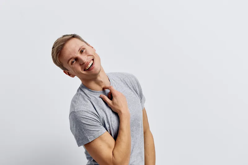 Happy smiling young caucasian man in gray t-shirt touch neck look camera isolated on white background digital detox concept joy and mental health
