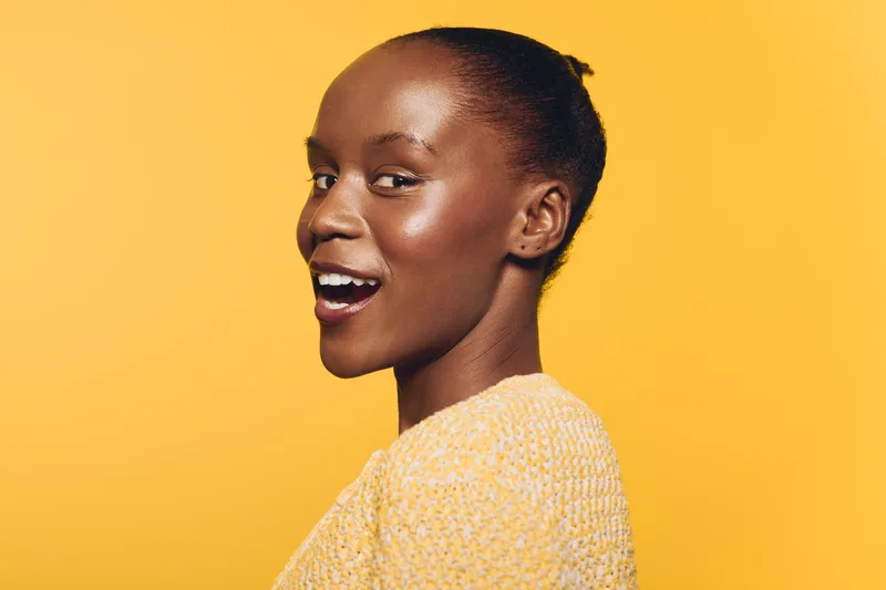 Smiling African woman with dark skin wears yellow sweater against bright yellow background. Side profile portrait with natural makeup and joyful expression. Concept of happiness and beauty.
