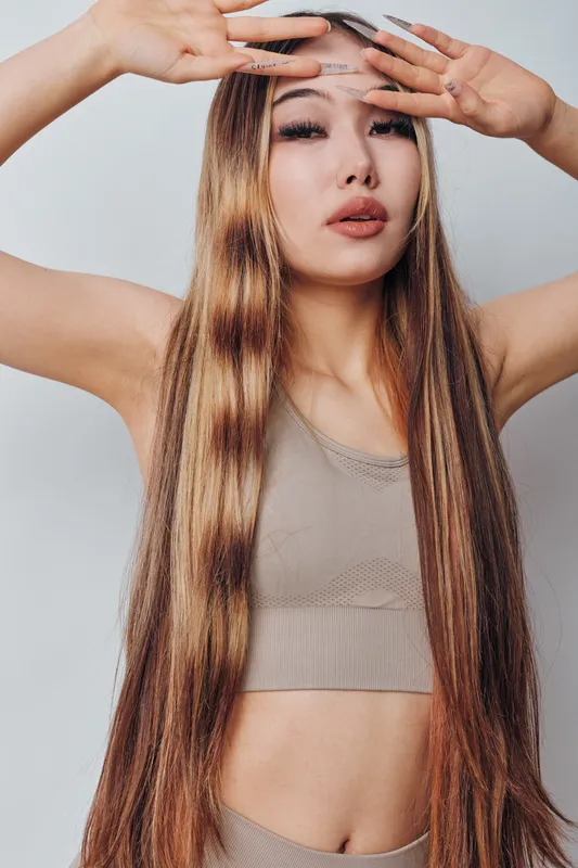 Young woman with long straight hair posing with hands near face wearing sleeveless top studio portrait beauty fashion and style with confident expression.