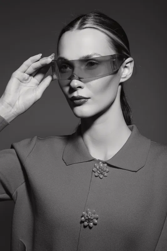 Young white woman with pale skin wearing futuristic glasses and stylish outfit poses in studio, showcasing fashion and modern eyewear concept.