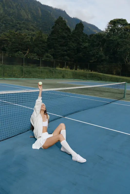 Young woman in sporty attire playing tennis on a blue court, showcasing joy and enthusiasm amidst a vibrant green backdrop
