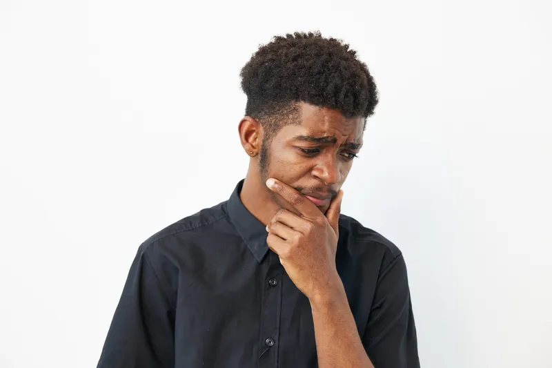 Pensive black man contemplating ideas while wearing a black shirt, showcasing deep thought and reflection in a minimalist background.