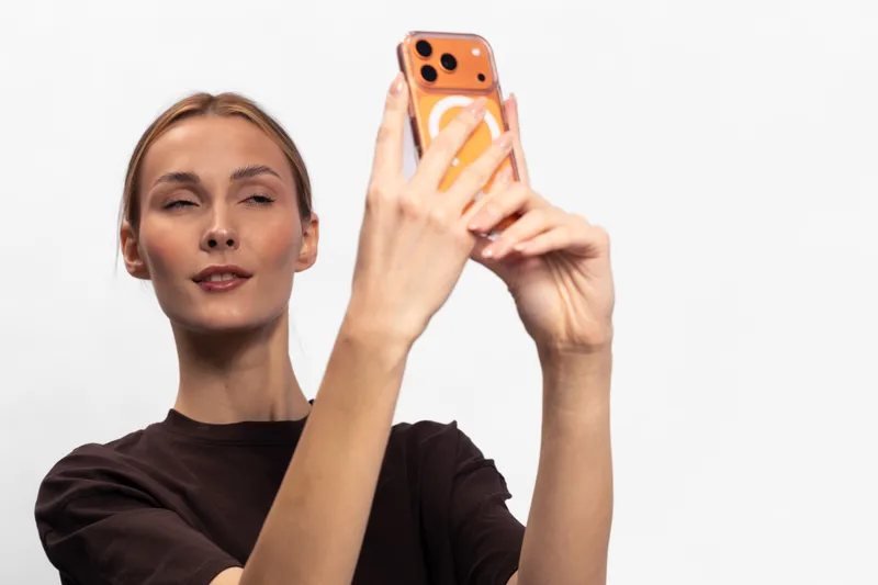 Young woman with fair skin and blonde hair takes a selfie with a smartphone on a white background. Concept of technology, communication, and social media usage.