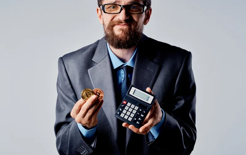 Бизнесмен с калькулятором в руках и криптовалютой Bitcoin, курс обмена богатства
