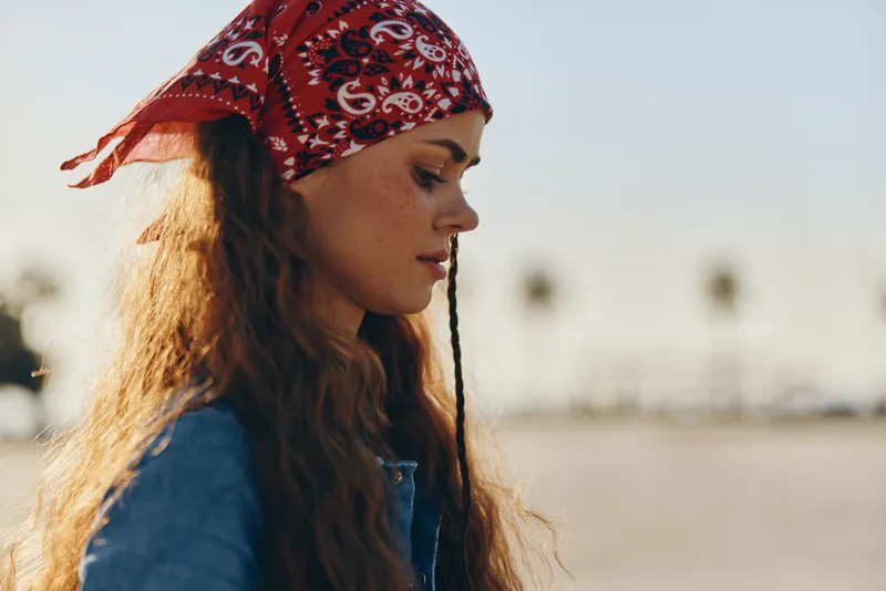 side view of young woman wearing red bandana and denim jacket outdoors with blurred background in warm natural light, casual style and serene mood