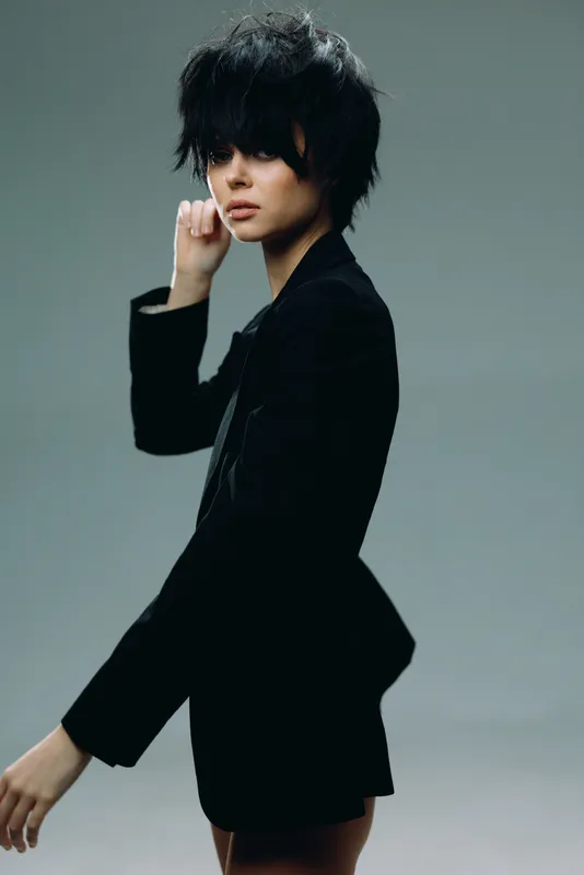stylish woman with short black hair wearing a black blazer in a minimalistic studio setting