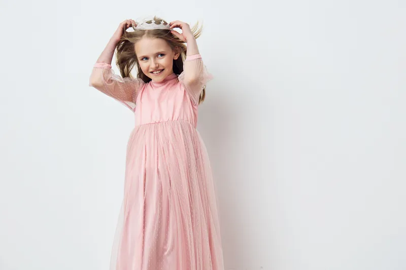 Young girl in a pink tulle dress posing happily against a white background, showcasing joy and innocence, ideal for children s fashion and portrait photography