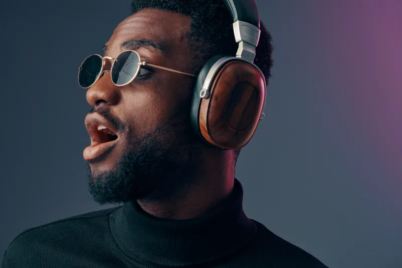 Young African man wearing stylish headphones and sunglasses, enjoying music with a vibrant background and expressive emotions