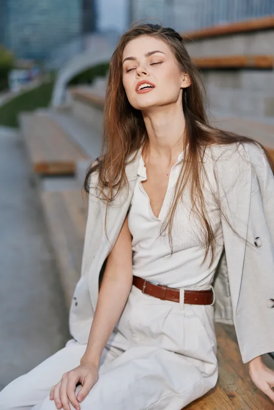 Businesswoman in stylish outfit exuding confidence and elegance, seated outdoors with a modern urban backdrop showcasing her professional demeanor and relaxed expression.