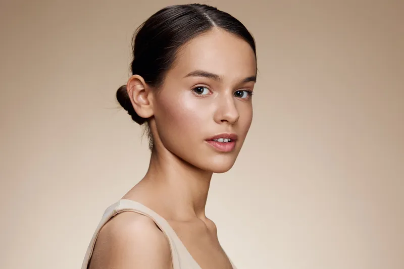 Portrait of a young woman with smooth skin and a natural expression, showcasing minimalistic fashion against a soft beige background KEY young, woman, portrait, beauty, smooth, natural, minimalism,