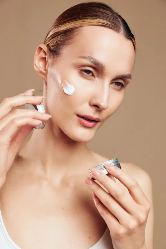 Bright closeup of a woman applying cream to her cheek, showcasing a skincare routine, soft lighting, smooth complexion, calm expression, neutral background with soft tones and natural colors,