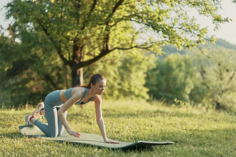 Young athletic woman practicing yoga on a mat in a lush green park, wearing comfortable sportswear, exuding calmness and focus in a seasonal spring setting