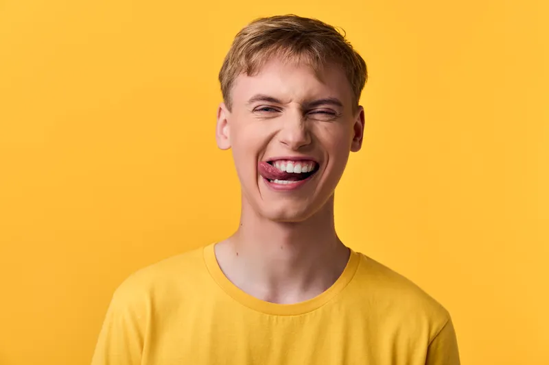 Man, laughter and bright yellow background convey cheerful energy, happiness, and a joyful mood in a candid studio moment, creating a friendly, lighthearted vibe and warm, approachable atmosphere