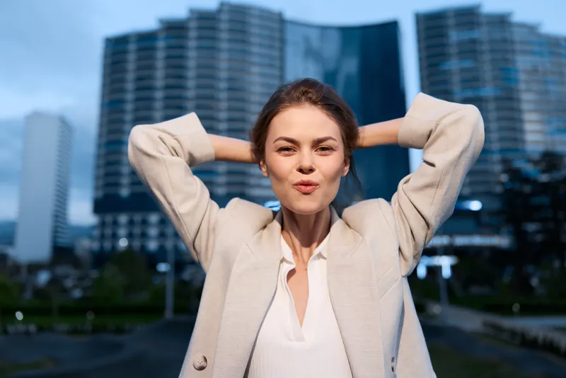 confident woman in beige blazer with modern cityscape background expressing calm confidence and stylish business fashion mood