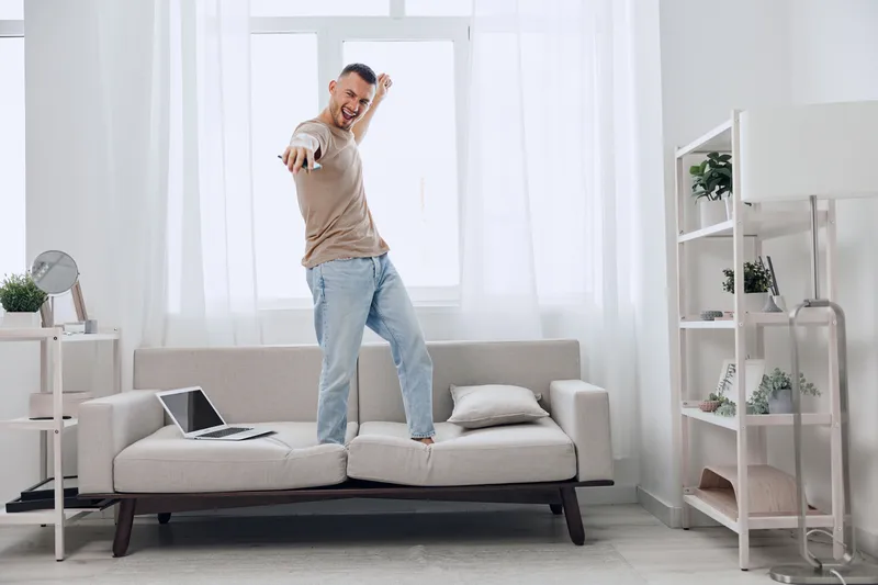 Energetic man dancing on couch, embracing digital detox while enjoying a creative moment. A vibrant expression of joy amidst the chaos of modern life.