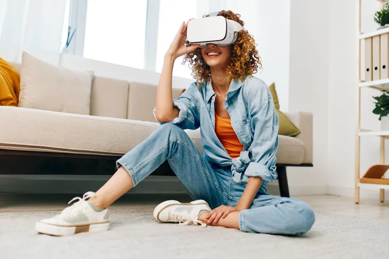 Женщина улыбается, используя VR-очки, и наслаждается футуристической кибер-игрой дома, испытывая счастье от виртуальной реальности