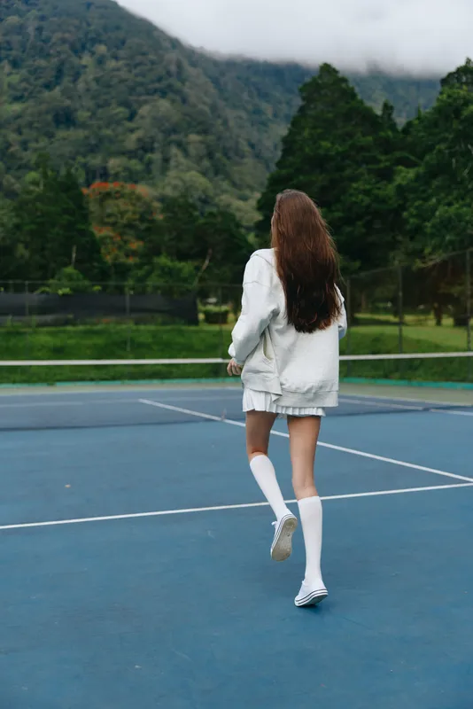 Young woman in sports attire running on a tennis court, showcasing energetic vibes and healthy lifestyle amidst a natural backdrop