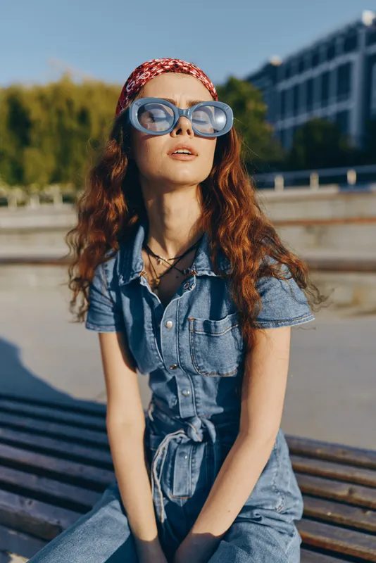 Lifestyle woman in modern boho-western denim street style wearing oversized sunglasses and a red headband, captured with warm film color tones on a sunny day.