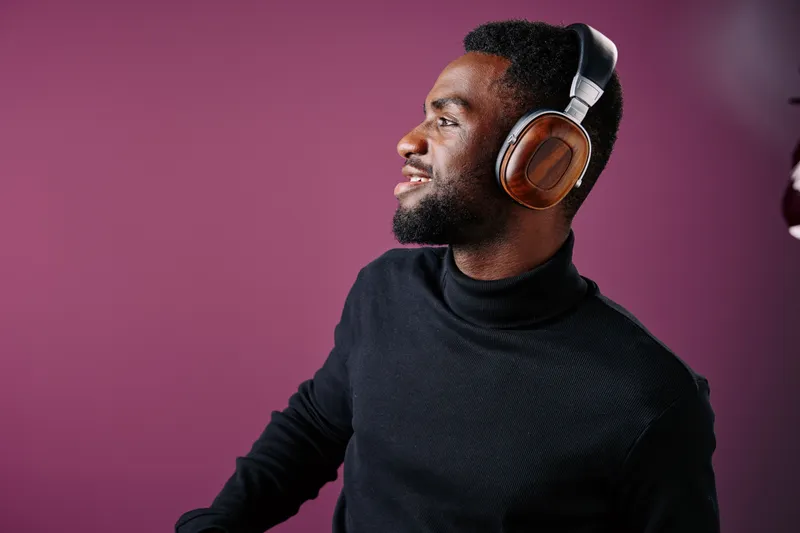 Young Black man smiling while wearing stylish headphones against a vibrant purple background, showcasing modern fashion and enjoyment of music