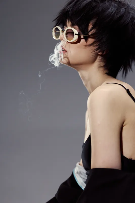 Young Asian woman wearing round sunglasses smoking with gray background and modern style.