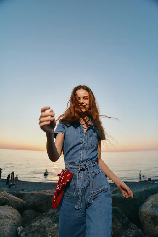 lifestyle woman in modern boho-western denim street style enjoying sunset by the sea with film color tones and relaxed, joyful expression
