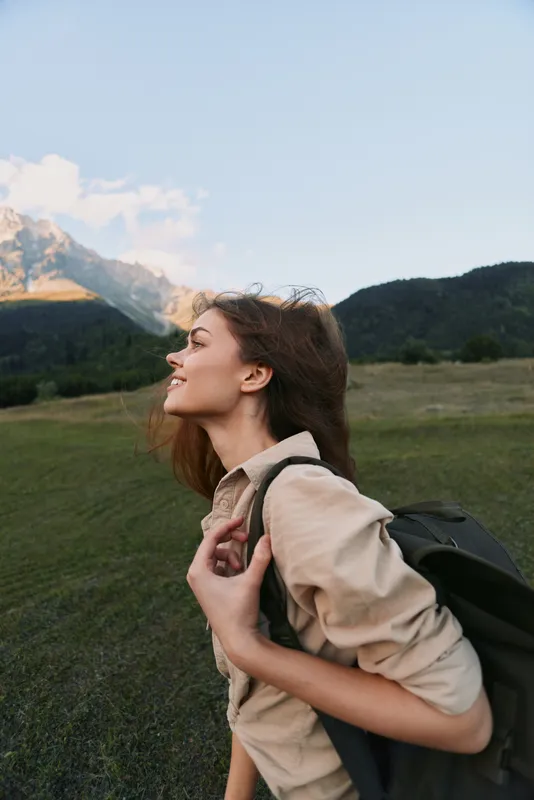 Young woman traveler with backpack enjoys fresh air and mountain view during hiking trip in nature landscape, feeling relaxed and happy outdoors lifestyle.