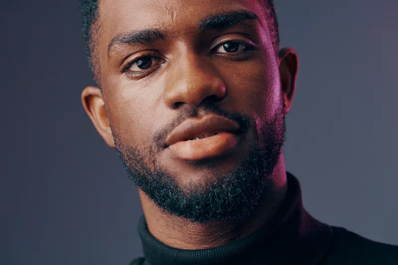 Portrait of a smiling African man in a black turtleneck against a softly lit background, conveying confidence and style