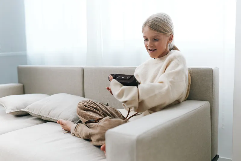 Authentic scene of a young girl playing a game at home on a light sofa, capturing a casual lifestyle and playful moment linked to school routines.