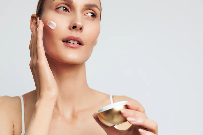 Woman applying face cream, closeup studio portrait on white background, skincare beauty wellness concept, soft studio lighting, calm facial care routine, smooth skin