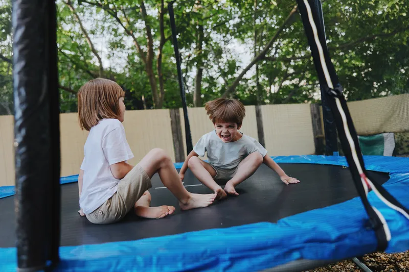 Two playful children enjoying a fun time on a trampoline, surrounded by lush greenery and bright sunlight. Capturing the joy of childhood and active play.